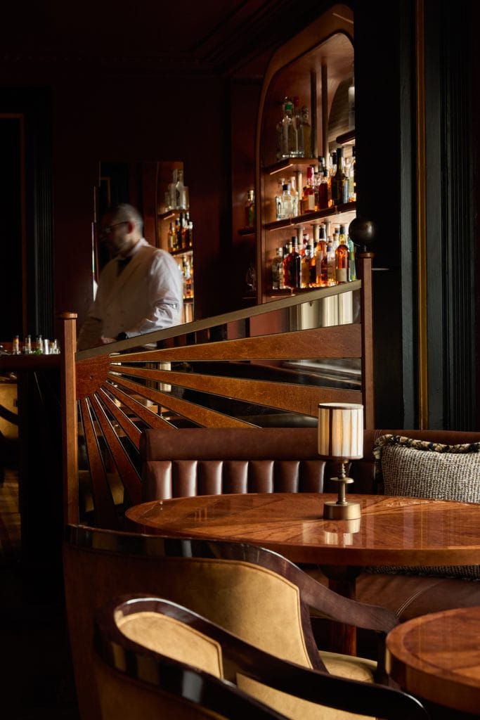 Bartender at the back bar behind the timber balustrade at Simpson's Bar, London
